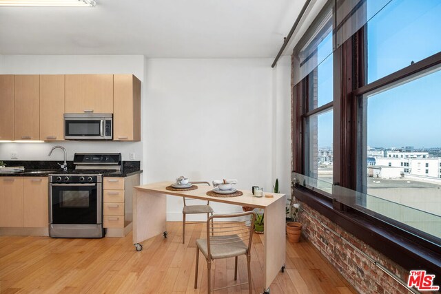 kitchen with brick wall, light brown cabinets, stainless steel appliances, and light wood-type flooring