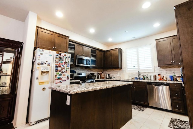 kitchen with light stone countertops, appliances with stainless steel finishes, dark brown cabinetry, a kitchen island, and backsplash