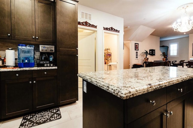 kitchen with light stone countertops, a notable chandelier, hanging light fixtures, and dark brown cabinets