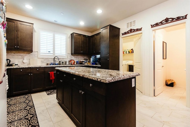 kitchen featuring tasteful backsplash, dark brown cabinets, light stone countertops, a kitchen island, and sink