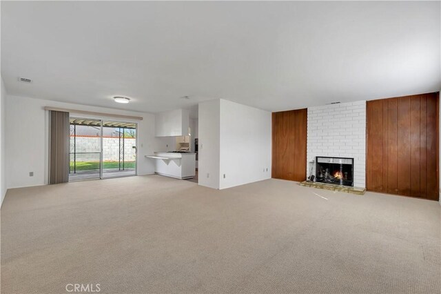 unfurnished living room with light colored carpet, a fireplace, and wood walls