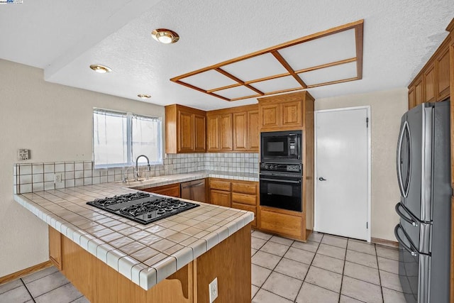 kitchen featuring light tile patterned flooring, tasteful backsplash, black appliances, tile counters, and kitchen peninsula