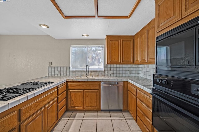 kitchen featuring tasteful backsplash, tile counters, sink, and black appliances