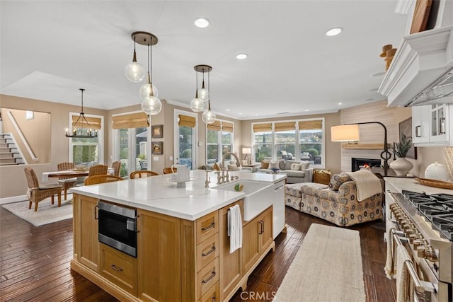 kitchen with a center island with sink, high end stove, dark hardwood / wood-style floors, pendant lighting, and sink