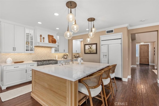 kitchen with white cabinetry, paneled refrigerator, an island with sink, decorative light fixtures, and light stone countertops