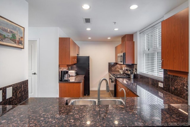 kitchen featuring backsplash, kitchen peninsula, sink, appliances with stainless steel finishes, and dark stone counters