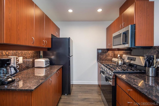 kitchen featuring decorative backsplash, appliances with stainless steel finishes, dark hardwood / wood-style flooring, and dark stone counters