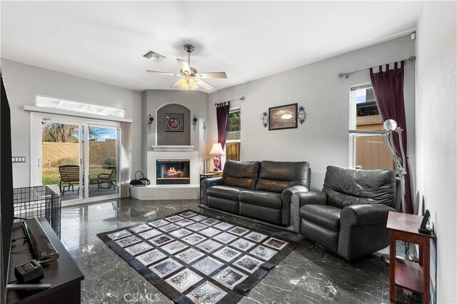 living room featuring ceiling fan, a healthy amount of sunlight, and a fireplace