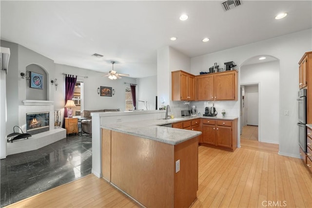 kitchen featuring ceiling fan, kitchen peninsula, light stone counters, and sink