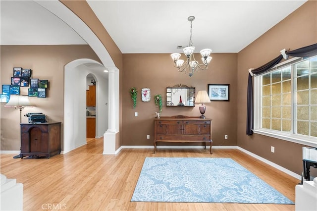 entryway featuring light wood-type flooring, an inviting chandelier, and decorative columns