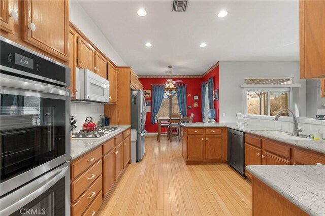 kitchen with backsplash, pendant lighting, kitchen peninsula, sink, and appliances with stainless steel finishes