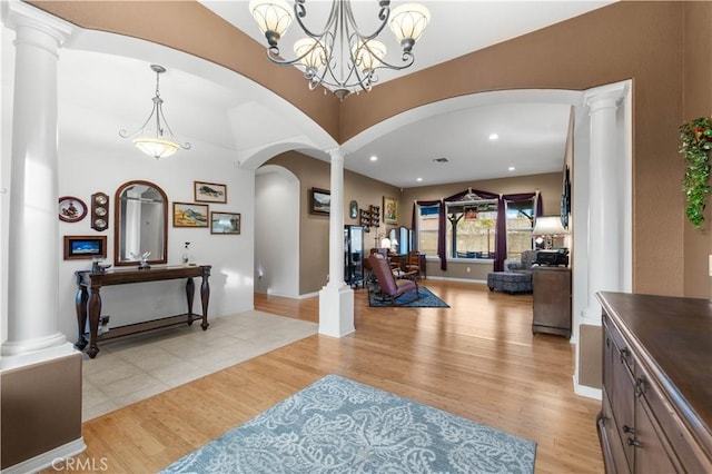 foyer entrance featuring a notable chandelier, light hardwood / wood-style floors, and decorative columns