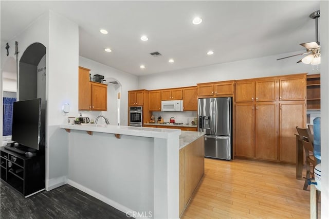 kitchen featuring ceiling fan, light hardwood / wood-style floors, a kitchen bar, kitchen peninsula, and stainless steel appliances