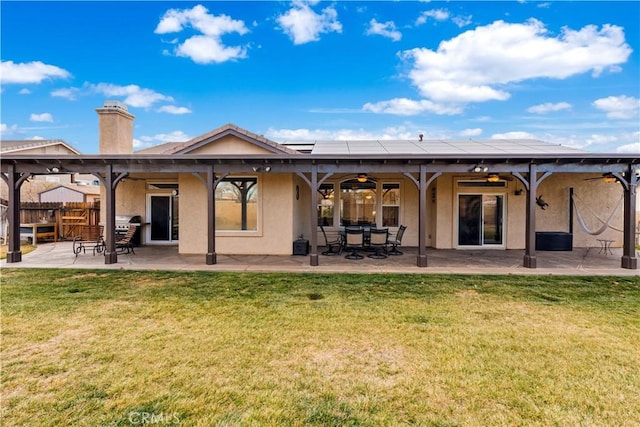 back of property featuring a patio area, ceiling fan, a lawn, and solar panels