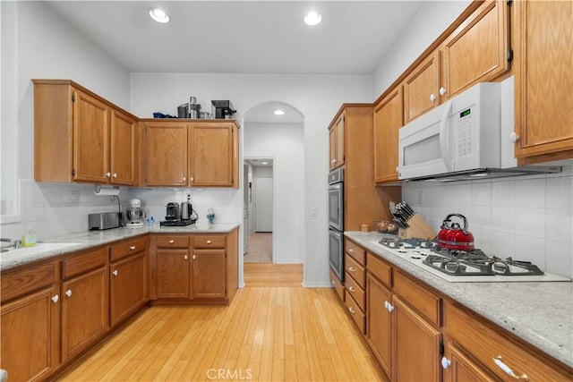 kitchen with decorative backsplash, light stone countertops, white appliances, and light hardwood / wood-style flooring