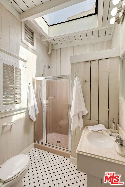 bathroom featuring a shower with shower door, beamed ceiling, and wooden walls