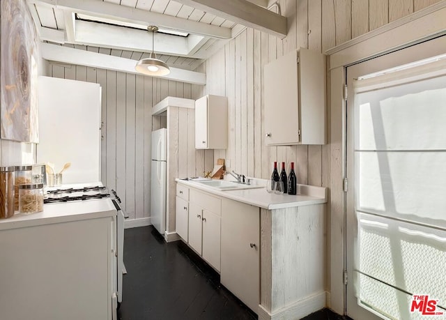 kitchen featuring white appliances, white cabinetry, sink, wood walls, and beam ceiling