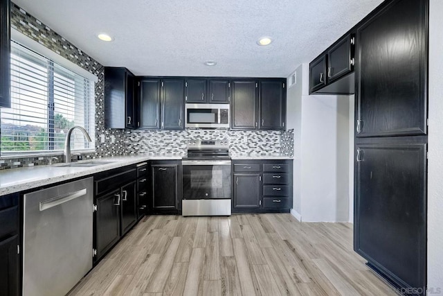 kitchen with a textured ceiling, appliances with stainless steel finishes, tasteful backsplash, light hardwood / wood-style floors, and sink