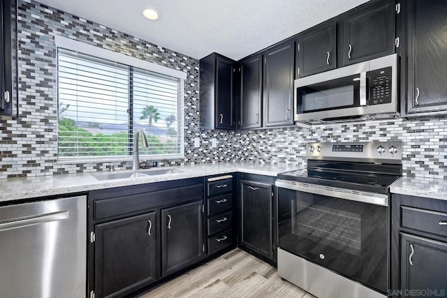 kitchen featuring tasteful backsplash, sink, light hardwood / wood-style flooring, light stone countertops, and stainless steel appliances