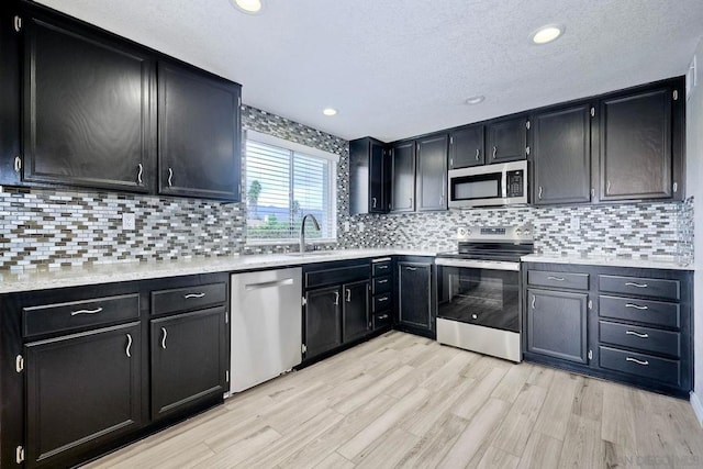 kitchen with sink, backsplash, stainless steel appliances, and light wood-type flooring