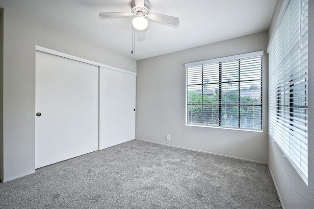 unfurnished bedroom with ceiling fan, a closet, multiple windows, and carpet flooring