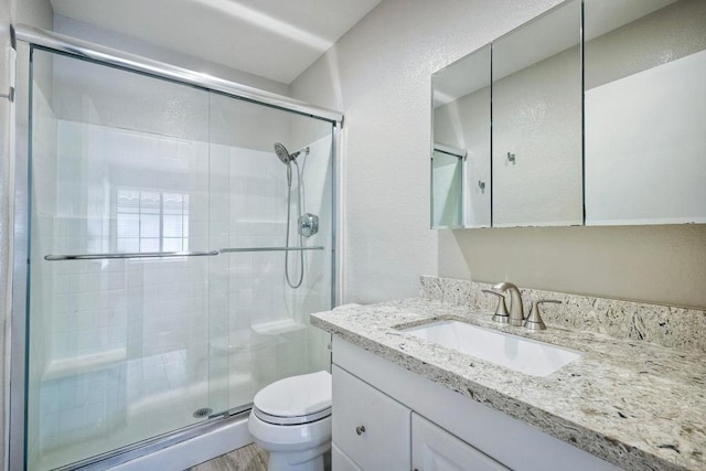 bathroom with a shower with shower door, toilet, and vanity