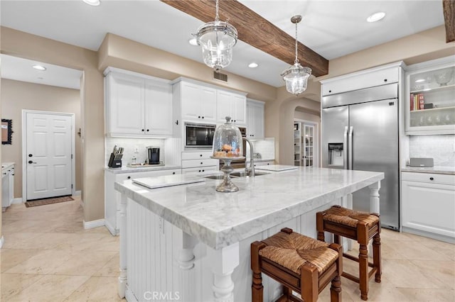 kitchen featuring white cabinetry, pendant lighting, built in appliances, and an island with sink