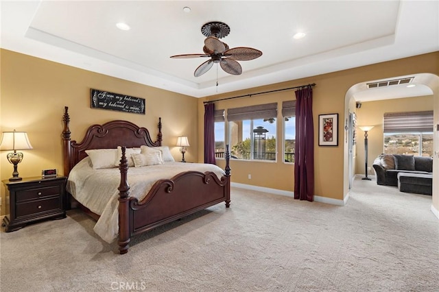 bedroom featuring a tray ceiling, light colored carpet, and ceiling fan