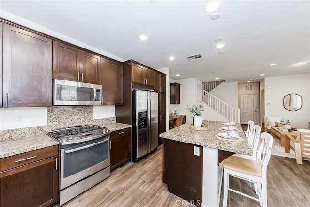 kitchen with light stone countertops, appliances with stainless steel finishes, a kitchen island, light hardwood / wood-style flooring, and a breakfast bar area