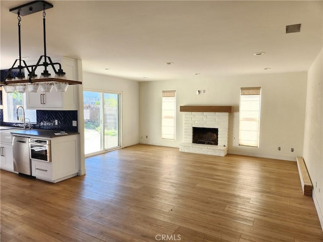 kitchen with a fireplace, decorative backsplash, white cabinetry, light wood-type flooring, and stainless steel appliances