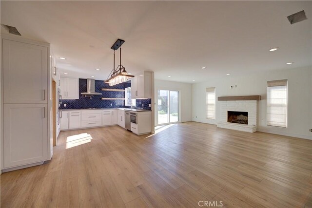 kitchen with white cabinetry, light hardwood / wood-style floors, a stone fireplace, tasteful backsplash, and range hood