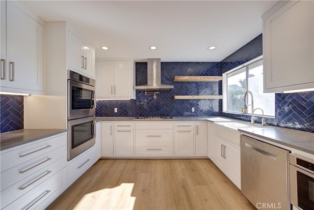 kitchen featuring backsplash, white cabinets, wall chimney exhaust hood, and appliances with stainless steel finishes