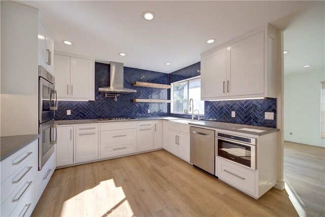 kitchen with backsplash, white cabinetry, light wood-type flooring, appliances with stainless steel finishes, and ventilation hood