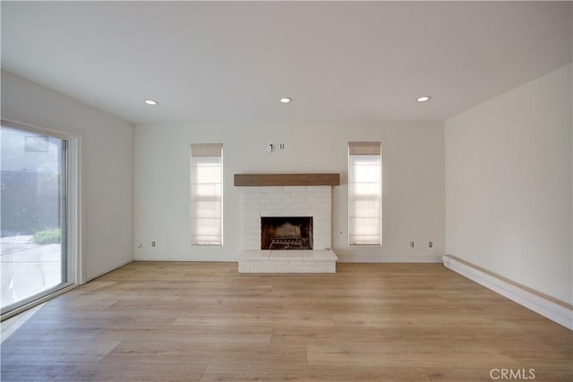 unfurnished living room featuring a healthy amount of sunlight, a brick fireplace, and light hardwood / wood-style floors