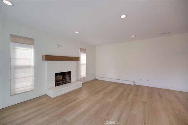 unfurnished living room featuring light wood-type flooring, baseboard heating, and a brick fireplace