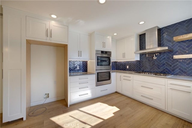 kitchen featuring appliances with stainless steel finishes, wall chimney exhaust hood, white cabinets, and tasteful backsplash