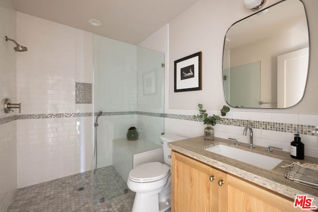 bathroom featuring tile walls, toilet, vanity, and a tile shower