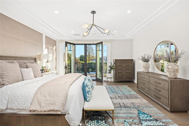 bedroom featuring light wood-type flooring, access to exterior, a raised ceiling, and a notable chandelier