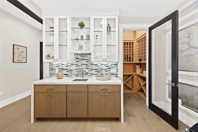 bar featuring light hardwood / wood-style floors, tasteful backsplash, and sink