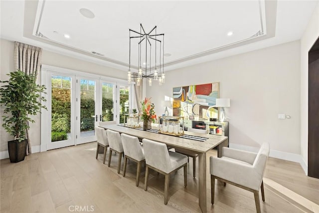 dining space featuring a tray ceiling, french doors, and light wood-type flooring