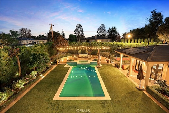 pool at dusk with a lawn, an outdoor hangout area, and a patio area