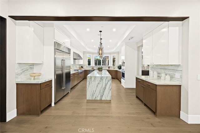 kitchen featuring stainless steel appliances, white cabinets, a kitchen island, and light stone countertops