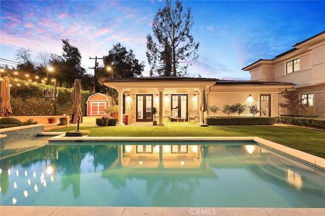 pool at dusk featuring a yard and a storage shed