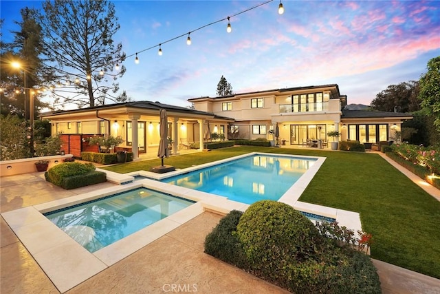 back house at dusk with a pool with hot tub, a balcony, a yard, and a patio