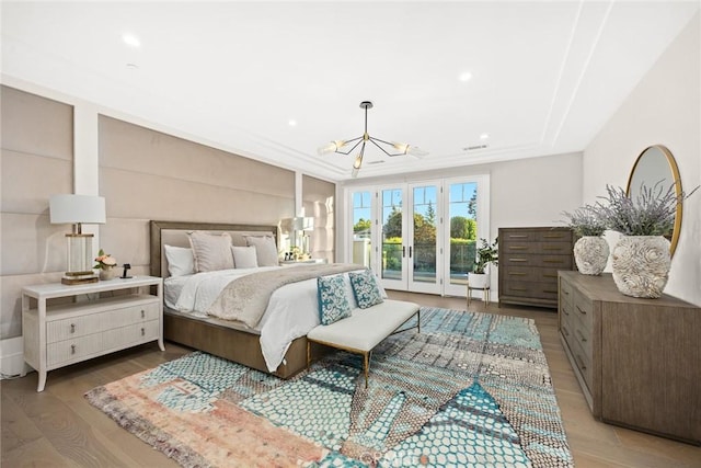 bedroom featuring light wood-type flooring, access to exterior, a notable chandelier, and a tray ceiling