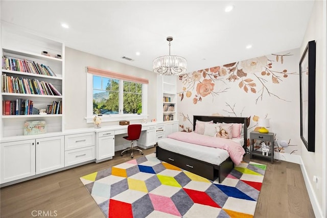 bedroom with built in desk, an inviting chandelier, and light hardwood / wood-style floors