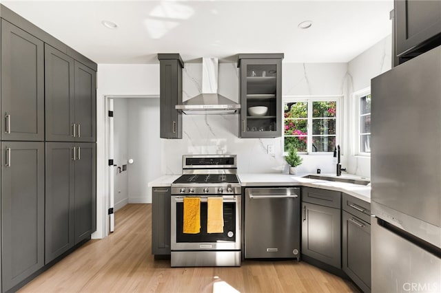 kitchen with wall chimney exhaust hood, sink, stainless steel appliances, and light hardwood / wood-style flooring