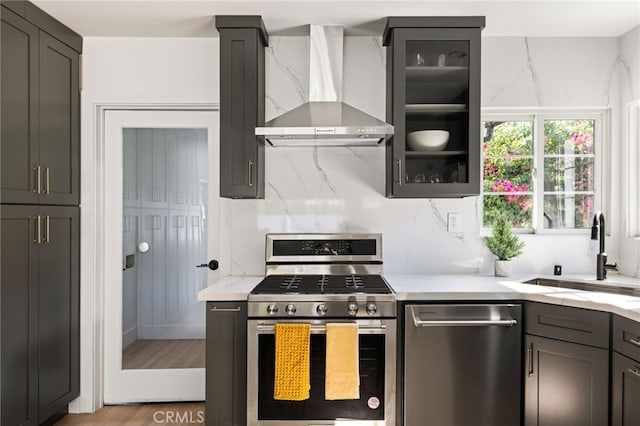 kitchen with wall chimney exhaust hood, stainless steel appliances, light hardwood / wood-style floors, sink, and backsplash