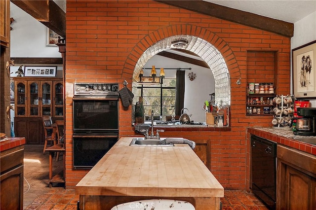 kitchen featuring brick wall, black dishwasher, lofted ceiling with beams, and multiple ovens