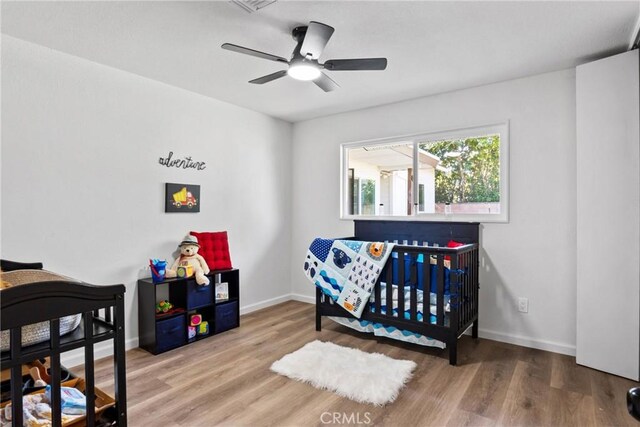 bedroom with ceiling fan, a crib, and hardwood / wood-style floors